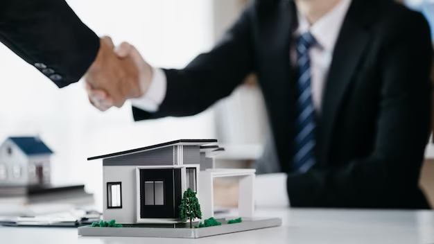 Two people in suits shaking hands next to a small house on a table